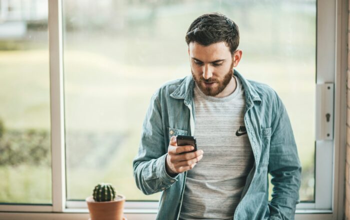 Man standing by a sunny window looking at his smartphone