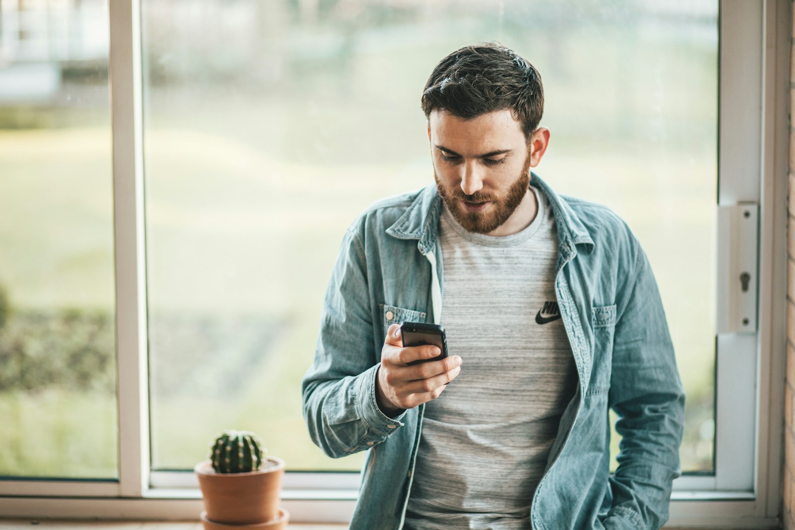 Man standing by a sunny window looking at his smartphone