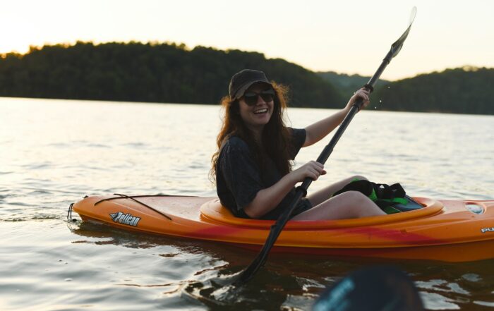 Smiling woman paddling a kayak on a calm lake surrounded by forested hills