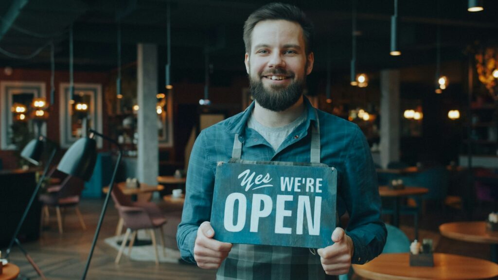 Smiling cafe owner holding a sign that reads Yes We're Open
