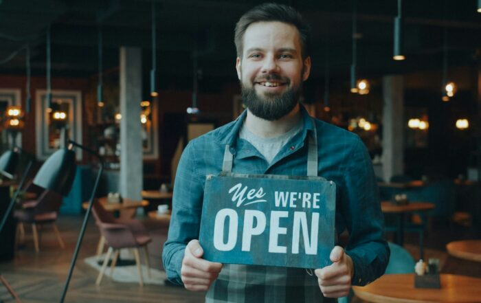 Smiling cafe owner holding a sign that reads Yes We're Open