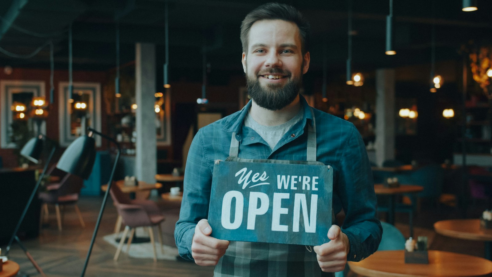 Smiling cafe owner holding a sign that reads Yes We're Open
