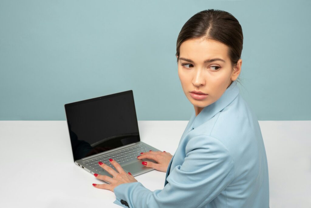 Woman at a laptop glancing over her shoulder with a cautious expression