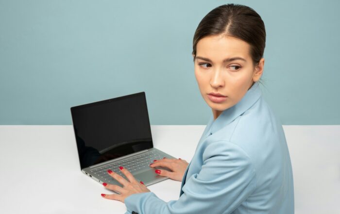 Woman at a laptop glancing over her shoulder with a cautious expression