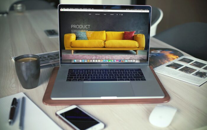 Laptop displaying an online store product page featuring a yellow sofa, next to a coffee mug