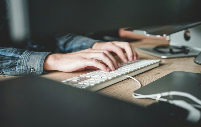Hands typing on a white keyboard at a wooden desk