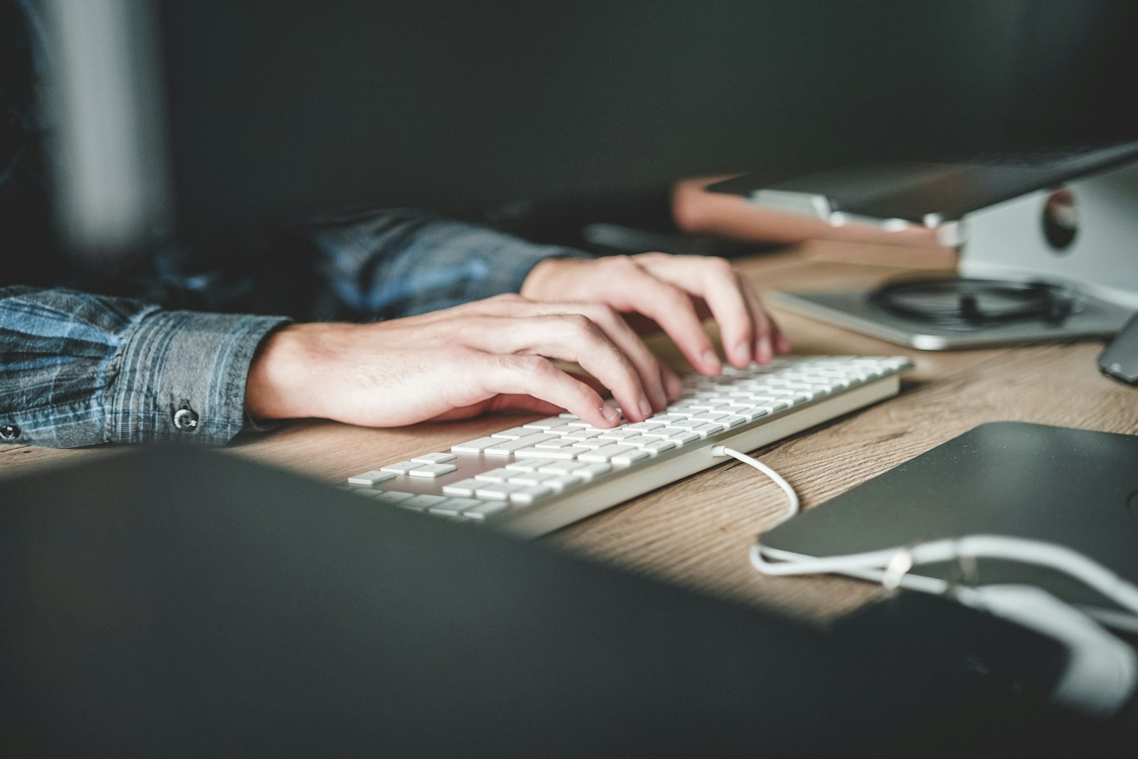 Hands typing on a white keyboard at a wooden desk
