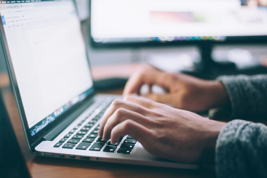 Person typing on a laptop at a desk with a second monitor in the background