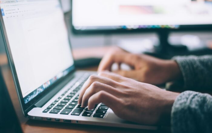 Person typing on a laptop at a desk with a second monitor in the background