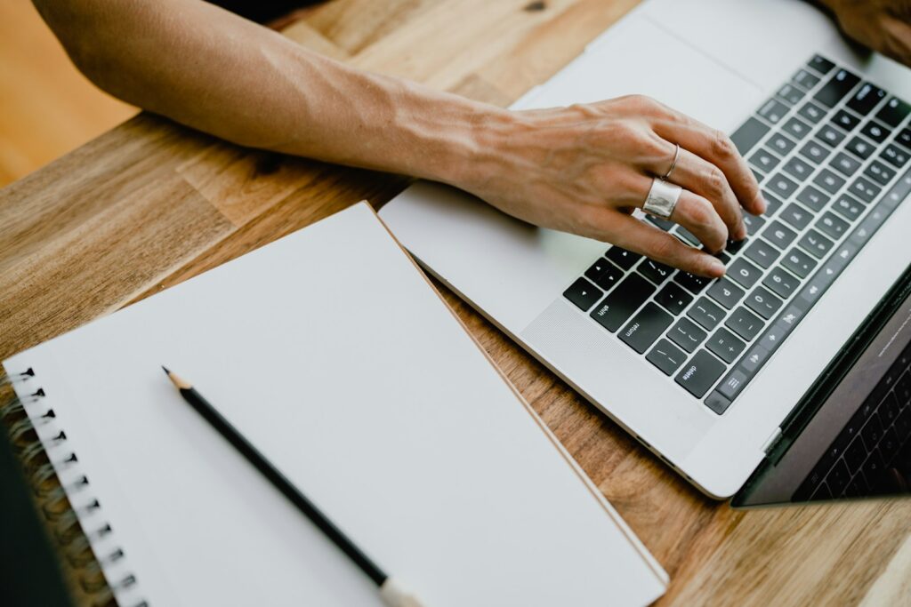 Person typing on a laptop next to a blank notepad and pencil