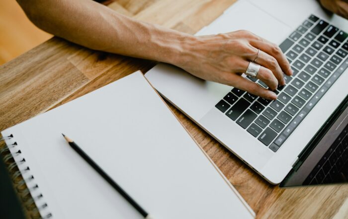 Person typing on a laptop next to a blank notepad and pencil